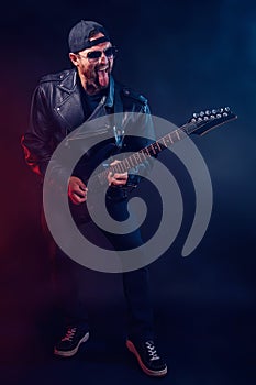 Full size photo of brutal bearded Heavy metal musician in leather jacket and sunglasses is playing electrical guitar