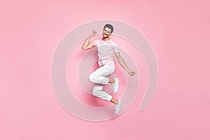 Full size photo of cheerful person raising fist smiling wearing t-shirt pants trousers isolated over pink background