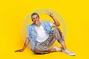 Full size photo of cheerful positive man dressed denim vest sit on floor showing v-sign symbol isolated on vibrant