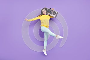 Full size photo of cheerful pretty happy woman jump up hold hands boombox isolated on purple color background
