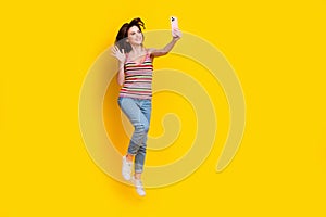 Full size photo of cheerful woman dressed knit top jeans jumping making selfie on smartphone say hi isolated on yellow