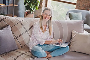Full size photo of clever young blond lady sit working laptop wear shirt jeans at home on weekend vacation alone