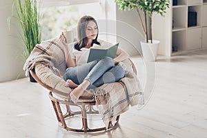 Full size photo of concentrated girl read book sitting on wicker chair with coffee cup wear white t-shirt in house