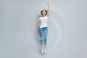 Full size photo of ecstatic overjoyed girl dressed white t-shirt denim jeans jumping hold fist up isolated on gray color