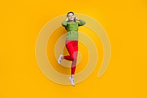 Full size photo of funky pretty lady jumping high holding ears with cool modern headphones listening music wear casual