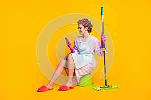 Full size photo of girl wash floor sit bucket use smartphone wear bath robe gloves isolated yellow color background