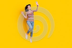 Full size photo of girlish woman dressed knit top jeans jumping making selfie on smartphone isolated on bright yellow