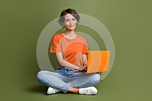 Full size photo of good mood cheerful woman wear t-shirt in glasses sit on floor with laptop working isolated on khaki