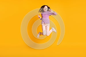 Full size photo of happy excited positive smiling little girl jumping show v-sign isolated on yellow color background