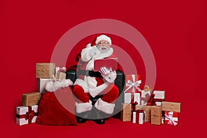 Full size photo of impressed santa sit buy gifts online index laptop wear cap glasses coat pants footwear isolated on