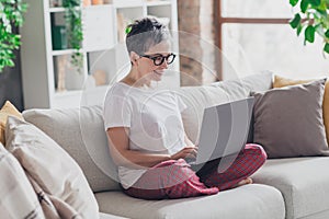 Full size photo of nice senior woman sit sofa netbook dressed white clothes cozy living room home house flat indoors