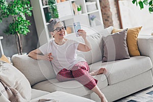 Full size photo of nice senior woman video call sit sofa dressed white clothes cozy living room home house flat indoors
