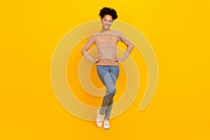 Full size photo of nice young brunette lady stand wear pullover jeans sneakers isolated on yellow color background