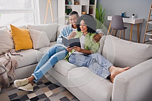 Full size photo of nice young man girl sit sofa hold notebook read book modern interior indoors cozy daylight apartment