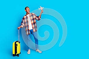 Full size photo of nice young man suitcase little plane empty space wear shirt isolated on blue color background