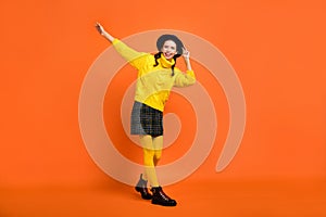 Full size photo of optimistic girl dance go wear yellow sweater cap skirt shoes isolated on orange background