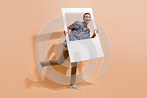 Full size photo of optimistic man wear print shirt brown trousers hold photo frame photographing isolated on beige color