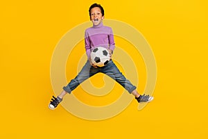 Full size photo of overjoyed energetic boy jumping hands hold football  on yellow color background