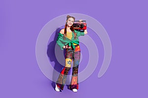 Full size photo of positive cute woman dressed green shirt print trousers hold boombox on shoulder isolated on purple