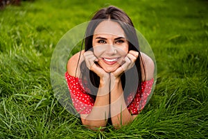 Full size photo of positive nice pretty woman lie grass hold hands cheekbones smile outside in park outdoors