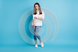 Full size photo of pretty lady long hairstyle confident person fixing sleeve white shirt jeans sneakers isolated blue