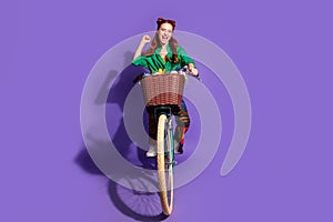 Full size photo of satisfied ecstatic woman dressed green shirt pants riding bike scream yeah win ride isolated on