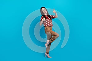 Full size photo of satisfied nice person wear red blouse brown trousers showing thumb up stand one leg  on blue