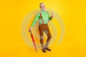 Full size photo of senior man happy positive smile hand touch suspenders parasol forecast isolated over yellow color