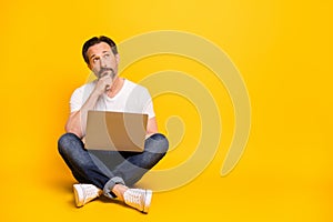 Full size photo of serious minded man sit floor hold laptop look empty space  on yellow color background