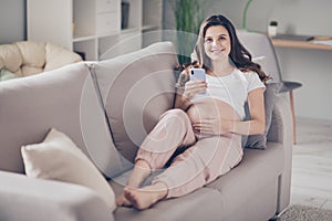 Full size photo of young attractive lovely happy smiling cheerful pregnant woman lying on couch use phone at home house