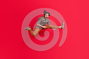 Full size photo of young crazy cheerful guy jumping playing guitar legs instrument isolated on red color background