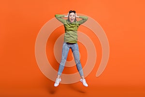 Full size photo of young excited crazy girl jump happy smile wow amazed news hands cover ears isolated over orange color