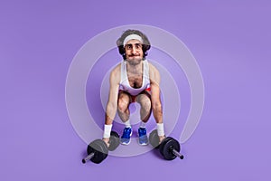 Full size photo of young funky funny crazy man in glasses trying to lift dumbbells isolated on purple color background photo
