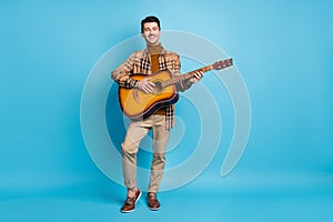 Full size photo of young handsome cheerful smiling positive man playing acoustic guitar  on blue color