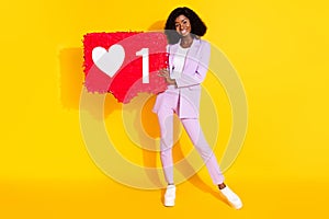 Full size photo of young happy afro girl hold demonstrate hug like reaction button isolated on yellow color background