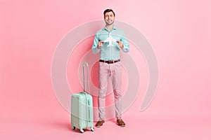 Full size photo of young happy cheerful positive smiling man with luggage hold paper plane isolated on pink color