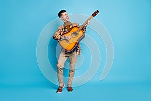 Full size photo of young happy positive good mood man playing acoustic guitar singing  on blue color background