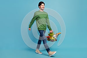 Full size photo of young smiling man go walk shopping buy groceries look copyspace isolated on blue color background