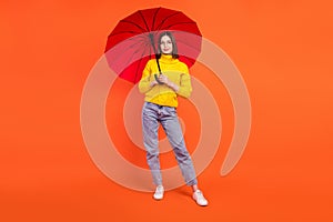 Full size photo of young woman happy positive smile walk rainy weather protection parasol isolated over orange color