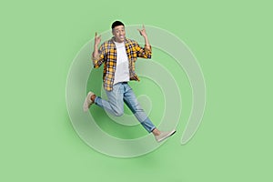 Full size portrait of carefree active sporty guy jump demonstrate heave metal symbol empty space isolated on green color