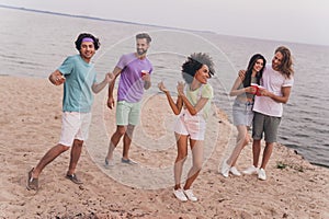 Full size portrait of excited positive fellows chilling dancing sand beach outside