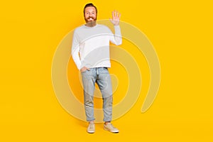 Full size portrait of friendly attractive man put arm pocket palm waving hello isolated on yellow color background