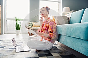 Full size profile photo of charming girl sit carpet floor hold notepad use laptop contemplate bright living room house
