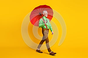 Full size profile side photo of aged man happy positive smile go walk wet rain parasol isolated over yellow color