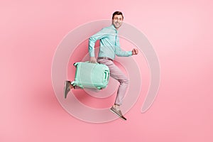 Full size profile side photo of brunette man hold luggage trip run jump wear teal shirt pink pants isolated on pastel