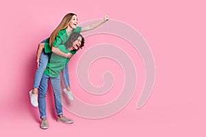 Full size profile side photo of couple teenagers playing together girl ride piggyback fist up to dream isolated on pink