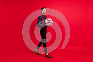 Full size profile side photo of young happy positive gentleman go walk hold flowers isolated on red color background