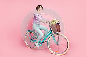 Full size profile side photo of young lovely pretty dreamy girl riding bicycle with flowers in basket isolated on pink