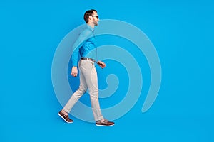 Full size profile side photo of young man happy positive smile go walk look empty space isolated over blue color