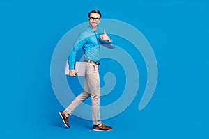 Full size profile side photo of young man happy smile go walk show thumb-up advert advise laptop isolated over blue